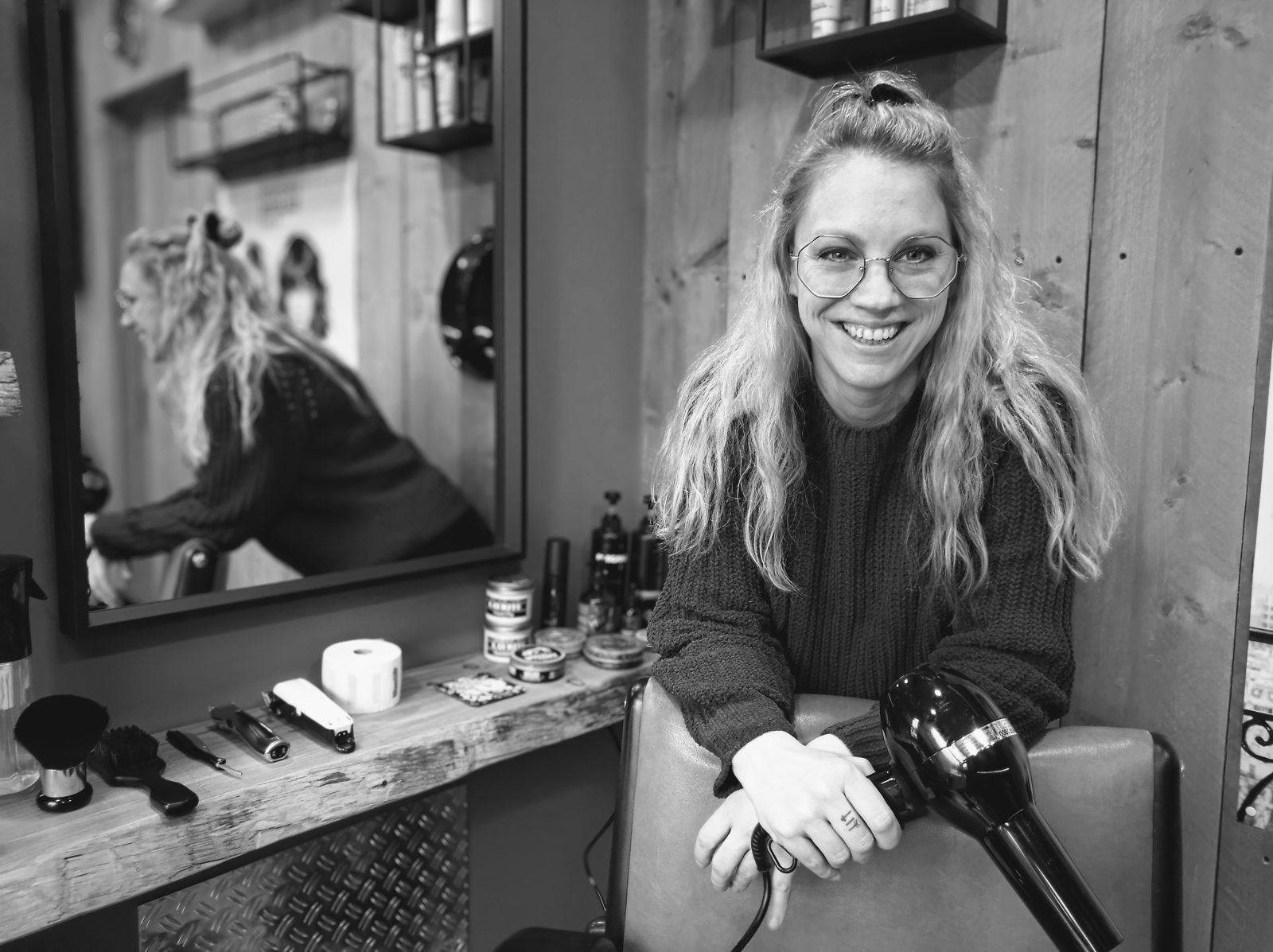 Patricia lachend in haar salon, leunend op de kappersstoel